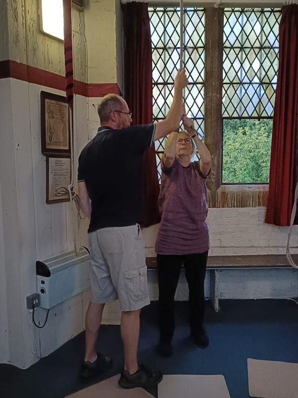 Ringing Master Jim Attwood, gives new ringer Emelia Thorold her first lesson in bellringing